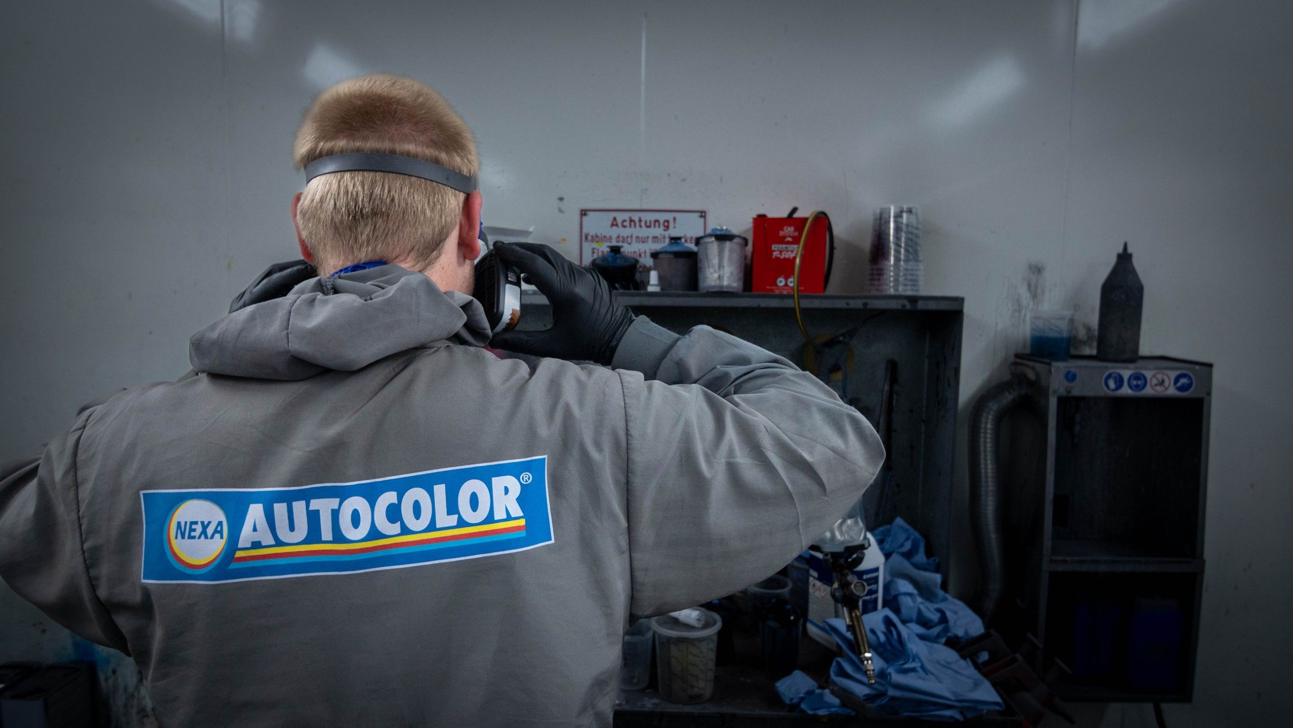 Rückansicht einer Person in grauem Schutzanzug mit Logo auf dem Rücken