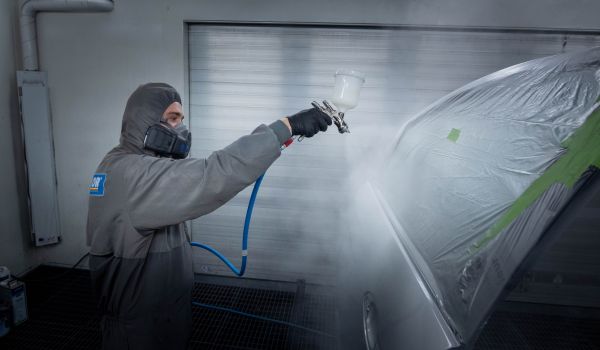Person in Schutzanzug beim Lackieren eines Autos mit Sprühwerkzeug